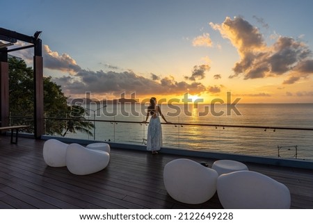 Beautiful woman in dress standing and enjoying the large balcony on sunset with sea view. Back view Royalty-Free Stock Photo #2122649228