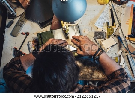 Overhead Photo of An Anonymous Carpenter Working in his Workshop. 
Table top view of unrecognizable man cutting a board on a table saw at his garage.