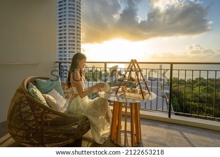Beautiful asian woman wearing dress enjoying afternoon tea and dessert at balcony on the sunset. Royalty-Free Stock Photo #2122653218