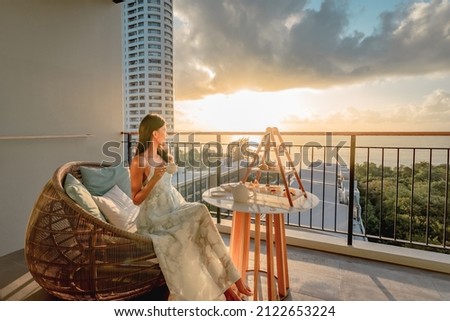Beautiful asian woman wearing dress enjoying afternoon tea and dessert at balcony on the sunset. Royalty-Free Stock Photo #2122653224