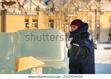 Portrait of a working assembler in a blue jacket and a knitted hat near the ice figure