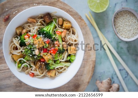 A bowl of Asian vegan noodles with broccoli, tofu, and peanuts