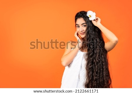 Spa and Wellness background with a beautiful indian woman with healthy long hair. She is dressed in a white towel, her hair is decorated with an orchid and she is looking at us. Royalty-Free Stock Photo #2122661171