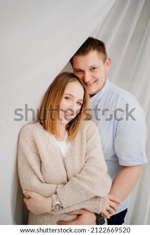 a happy and loving couple hugs against the background of a white curtain. cozy and beautiful clothes for the house. romantic relationships. psychological assistance to young families. Valentine's Day.
