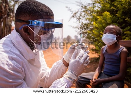 Doctor adjusts the syringe to inject the vaccine to an african child. Concept of covid-19 vaccination in Africa. Coronavirus vaccine. Royalty-Free Stock Photo #2122685423