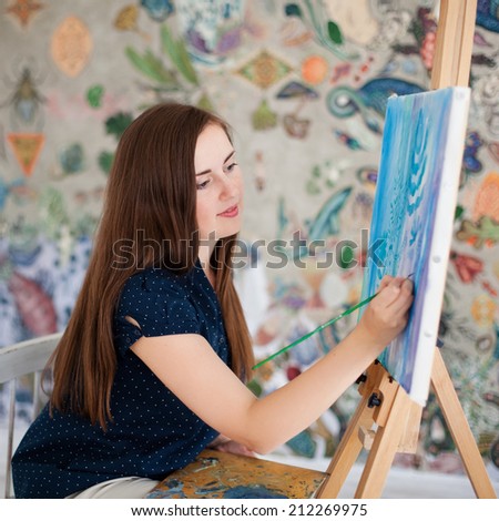 Young woman paints picture on canvas in her studio
