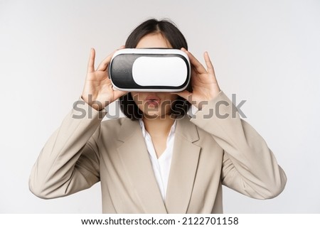 Amazed office woman, asian business person in suit, wearing vr headset, looking at smth in virtual reality glasses with impressed, wow face, white background