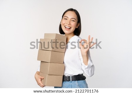 Portrait of beautiful happy woman carry boxes with orders. Businesswoman with carry delivery and showing okay sign, white background