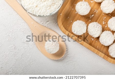 Coconut candy. Coconut balls on a wooden spoon and plate. Composition on light cement. Homemade vegan sweets. Close-up view, space for text. Delicious white balls of bliss. Royalty-Free Stock Photo #2122707395