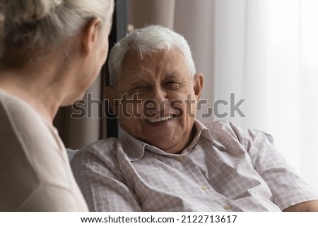 Happy elderly 80s man talking to wife, female carer at home, resting on couch, speaking to woman with toothy smile. Later life, old age, elderly care, marriage concept Royalty-Free Stock Photo #2122713617