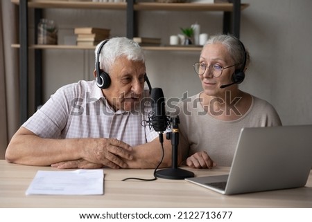 Old couple of bloggers in head sets streaming live video, broadcasting on air, using sound studio equipment, speaking at microphone, laptop computer, recording video interview, audio book