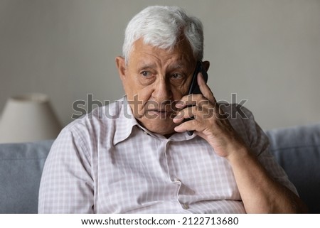 Serious concerned old grandpa talking on mobile phone, calling for emergency, ambulance. Senior 80s man speaking on cellphone, sitting on couch, at home, contact family on distance Royalty-Free Stock Photo #2122713680