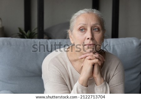 Sad lonely pensive elder lady looking away, sitting on couch at home with chin on hands, thinking over health problems, feeling sadness, boredom, apathy, concerned about memory loss, dementia Royalty-Free Stock Photo #2122713704