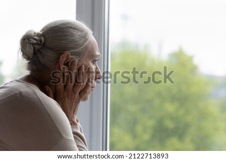 Upset lonely senior lady looking out of window with despair, frustration, going through depression, apathy, mental disorder, thinking over health problems, worried about memory loss, dementia Royalty-Free Stock Photo #2122713893