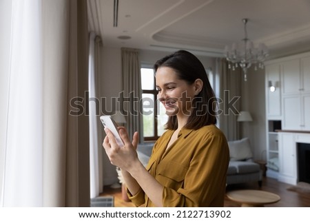 Side view happy beautiful young woman using cellphone applications, enjoying playing mobile games, web surfing, purchasing goods in internet store or communicating in social networks alone at home. Royalty-Free Stock Photo #2122713902
