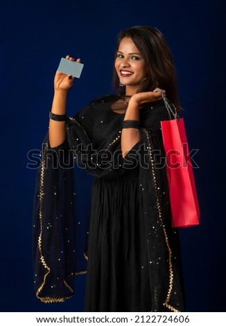 Beautiful young girl or woman holding and posing with shopping bags with credit or debit card on a dark background