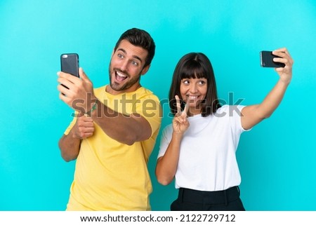 Young couple isolated on blue background making a selfie with mobile phone