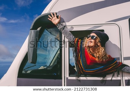 Overjoyed young adult woman oustretching arms outside the windows of a camper van and celebrate freedom and summer holiday travel vacation lifestyle Royalty-Free Stock Photo #2122731308