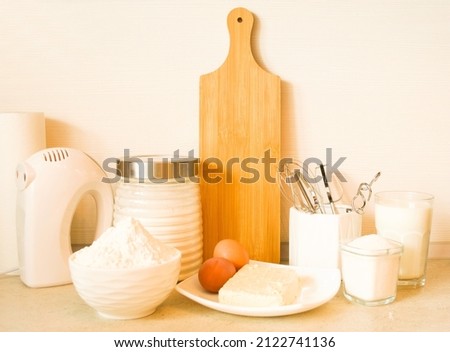 Food products for baking, glass jars with flour and sugar, a plate with eggs and butter, whisks, a mixer, a wooden board are on the table.  The concept of homemade food.  Photograph front view. 
