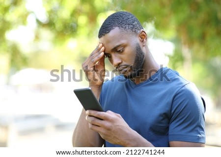 Worried man with black skin checking mobile phone standing in a park Royalty-Free Stock Photo #2122741244