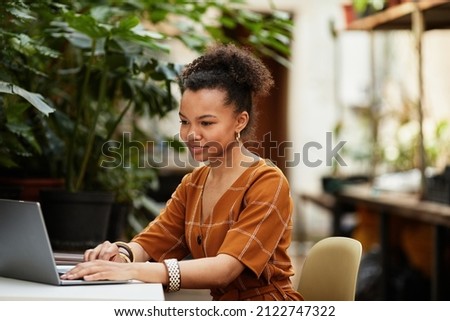 Happy young owner of modern orangerie or greenhouse sitting in front of laptop while looking through design trends online Royalty-Free Stock Photo #2122747322