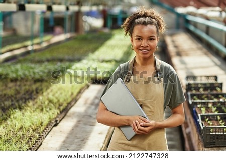 Pretty young African American female farmer or woner oh large hothouse with laptop standing against long tables with seedlings Royalty-Free Stock Photo #2122747328
