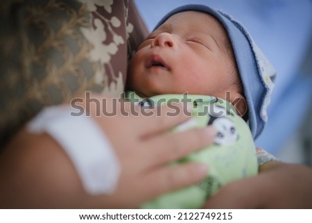 Newborn baby is sleeping on his mother's lap.