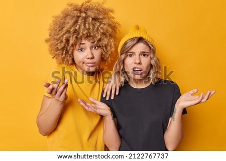 Uncertain women spread palms stand indignant cannot make decision shrug shoulders wear casual t shirts isolated over yellow background. Unsure hesitant female models feel questioned and clueless Royalty-Free Stock Photo #2122767737