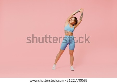 Full body young sporty fitness trainer woman wear blue tracksuit spend time in home gym tilt body to sides with hand stretch lunge exercise isolated on plain pink background. Workout sport concept. Royalty-Free Stock Photo #2122770068