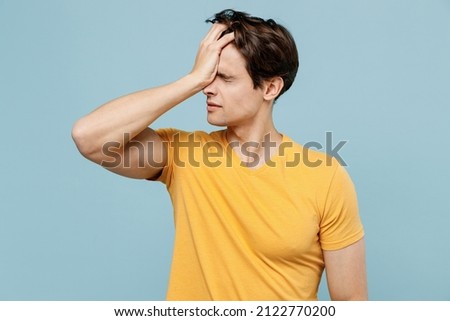 Young mistaken sad confused man 20s in yellow t-shirt put hand on face facepalm epic fail mistaken omg gesture isolated on plain pastel light blue background studio portrait. People lifestyle concept