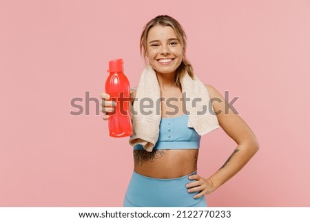 Young sporty athletic fitness trainer instructor woman wear blue tracksuit spend time in home gym give water bottle isolated on pastel plain light pink background. Workout sport motivation concept.