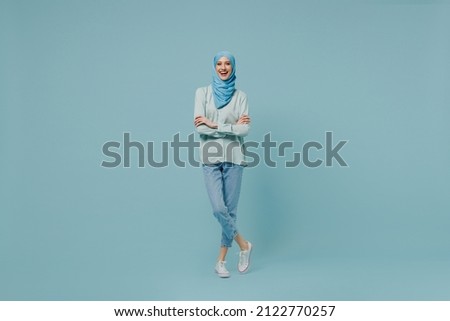 Full body young arabian asian muslim woman in abaya hijab hold hands crossed folded look camera isolated on plain blue background studio portrait. People uae middle eastern islam religious concept. Royalty-Free Stock Photo #2122770257