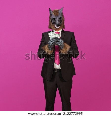 Against a pink background is a man dressed in a black suit with jacket, a white shirt and tie, wearing a werewolf mask, holding three 50 US dollar bills.