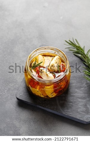 Homemade marinated feta cheese in glass jar with rosemary on dark board. Grey background
