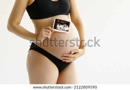 Prenatal ultrasound screening. Beauty pregnant holding sonogram picture of unborn baby inside her big belly. Happy expectant mom showing fetus usi scan image to camera