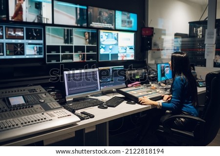 Beautiful middle aged beautiful woman working on a tv station as a producer in a broadcast control room. Show production maker. Television. Royalty-Free Stock Photo #2122818194