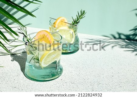 Summer refreshing lemonade drink or alcoholic cocktail with ice, rosemary and lemon slices on pastel light green surface. Fresh healthy cold lemon beverage. Water with lemon. Royalty-Free Stock Photo #2122824932