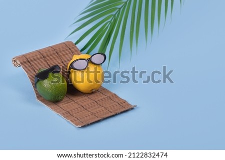 Creative fun idea with a lemon and lime in sunglasses lying on a sun bed on a bright blue background. Minimal travel and vacation concept, summer stylish tropical fruit. Summertime color mood. 