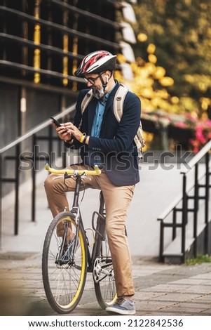 Successful middle-aged businessman using a smartphone on his way to work by bicycle  through the city.
