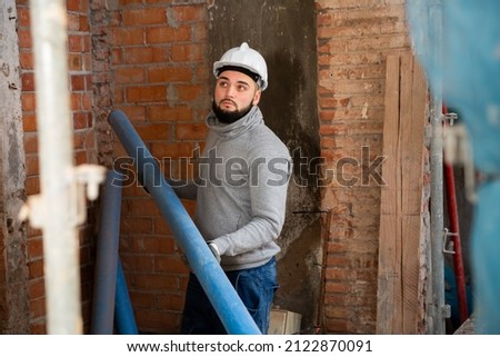 Focused bearded guy working with metal-reinforced plastic pipes at indoors building site