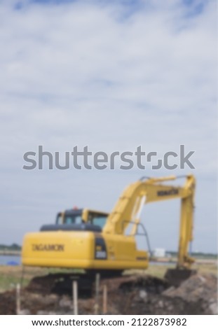 Yellow Komatsu excavator is digging the ground against a beautiful cloud background, blurred image. Royalty-Free Stock Photo #2122873982