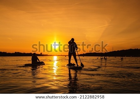 Silhouette of person standing up on sapboard on city river at sunset. Small local travel with family or friends, leisure and quality time outdoors.
