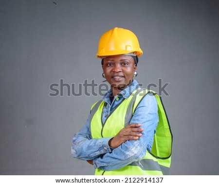 Studio portrait of an African Nigerian career lady or female engineer wearing a yellow safety helmet and a reflective jacket Royalty-Free Stock Photo #2122914137