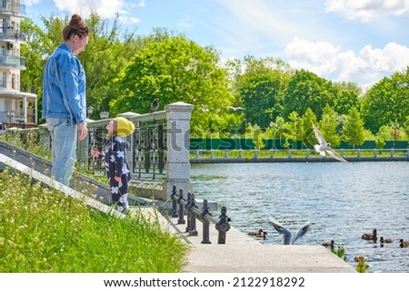 Mom and daughter feed bread crumbs to ducks and gulls on the city pond
