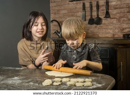 the boy helps his sister make cookies out of dough, his sister takes it off on a smartphone
