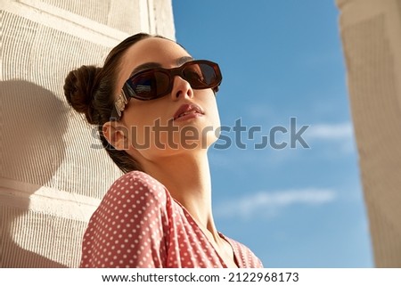 Outdoor portrait of a young beautiful confident woman posing on the street. Model wearing stylish sunglasses. Girl looking up. Female fashion. Sunny day. Close up. City lifestyle. Copy space for text Royalty-Free Stock Photo #2122968173