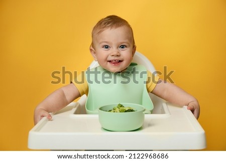Cute little baby wearing bib while eating on yellow background Royalty-Free Stock Photo #2122968686