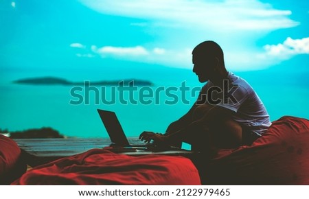 A silhouette portrait of a man working on his laptop with the background of the sea the sky and an island behind him Royalty-Free Stock Photo #2122979465