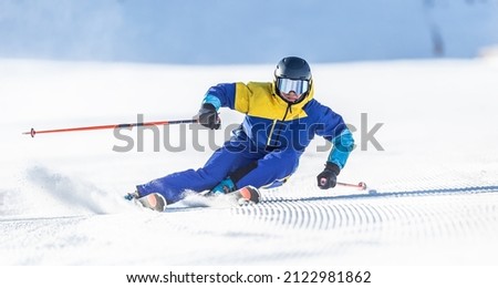 A young aggressive skier on an alpine slope demonstrates an extreme carving skiing style. He is skiing on morning perfectly groomed piste. Royalty-Free Stock Photo #2122981862