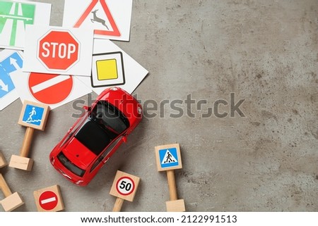 Many different road signs and toy car on grey background, flat lay with space for text. Driving school